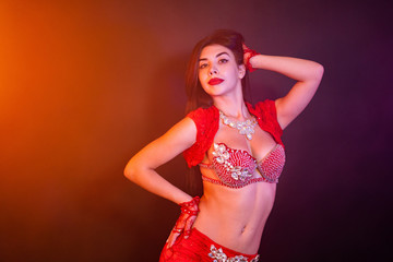 Tempting sexy traditional oriental belly dancer girl dancing on purple neon smoke background. Woman in exotic red costume sexually moves her semi-nude body.