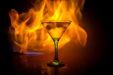 Martini in fire concept. Glass of famous cocktail Martini burning in fire at dark toned foggy background.