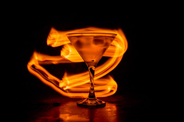Fototapeta na wymiar Martini in fire concept. Glass of famous cocktail Martini burning in fire at dark toned foggy background.