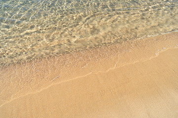 Beachline with bright orange-yellow sand and still transparent sea water in natural light at noon