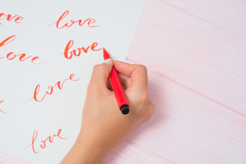 Calligrapher student practices in writing word LOVE with red marker on canvas. Creative artist...
