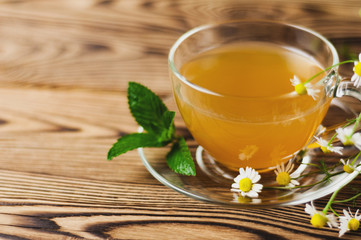 Full glass cup of green tea and mint and bunch of chamomile on old wooden table. Healthy concept