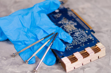 Blue rubber glove and three small metal screwdrivers near pc graphics card with copper radiator on old gray concrete floor