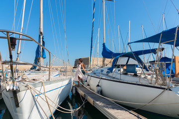 Fototapeta premium Elegant young tourist visitor woman walking on a sightseeing tour at Heraklion Venetian port, Crete, Greece . Venetian fortress Rocca A Mare or “Koule” at background