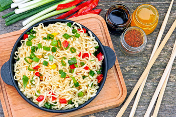 Chinese noodles in a cast-iron skillet on a wooden background.
