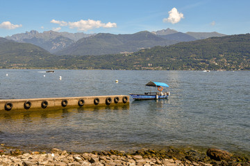 Molo sul lago con barca tipica, montagne sullo sfondo e cielo azzurro in estate, Isola dei Pescatori, Lago Maggiore, Piemonte, Italia
