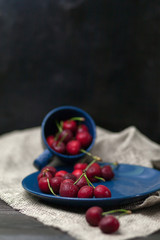 Cherries in the Cup, Juicy, fresh cherry with drops of water, in a blue Cup, on a blue plate, on a dark brown background, side view