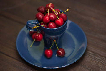 Cherries in the Cup, Juicy, fresh cherry with drops of water, in a blue Cup, on a blue plate, on a dark brown background, side view