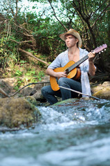 tourist with a guitar on vacation playing and singing over a forest river