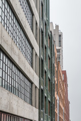 Looking down a city street at the 5th story level are many different styles of building. Some are modern and others are brick and historic, The day is gray, rainy and damp. Tall building are obscured.