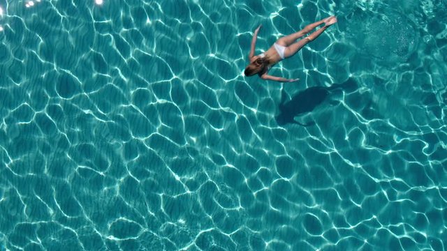 Aerial - Beautiful toned young woman in white bikini swimming underwater
