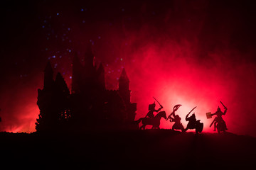 Medieval battle scene with cavalry and infantry. Silhouettes of figures as separate objects, fight between warriors on dark toned foggy background with medieval castle. Night scene. Selective focus