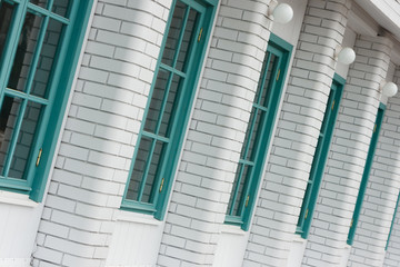 Colorful turquoise windows and detail of a house exterior on a white brick wall.