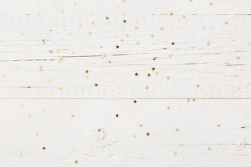 Top view on small golden stars confetti on old white wooden background.