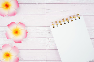 Creative arrangement of frangipani flowers and spiral notebook on a wooden texture background. Zen aromatherapy concept. Copy space on notebook for text.