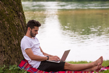 Fototapeta premium man using a laptop computer on the bank of the river