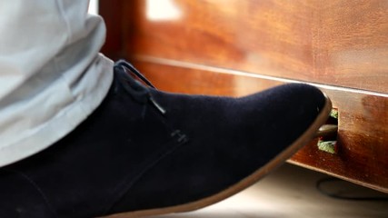 The foot of a man in blue suede shoe using sustain pedal on piano and then leaving.