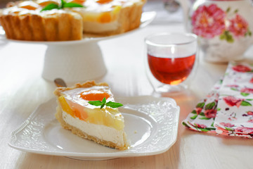 A slice of cheesecake with peaches and jelly on a table at teatime