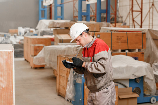 the storekeeper marks the arrival on the tablet. man driving a forklift through a warehouse in a factory. driver in uniform and protective helmet. the concept of logistics and storage