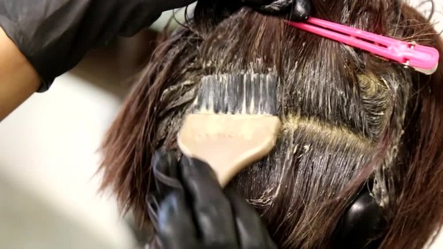Series of closeup of hair dresser applying chemical color dye onto hair of customer in salon 


