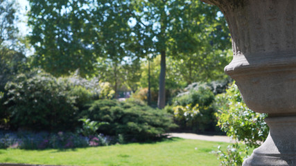 Out of focus background plate of public park with statue vase in foreground