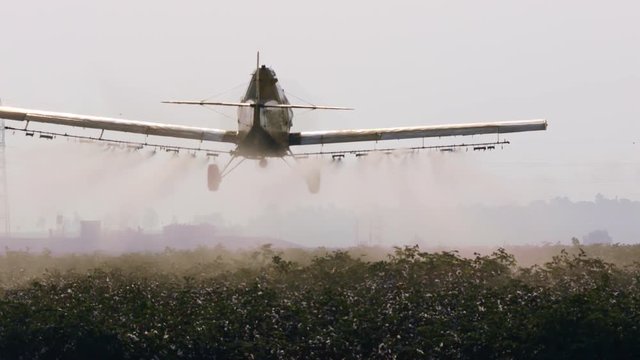 Crop duster spraying chemicals over a cotton field - slow motion