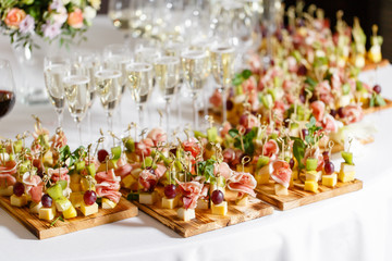 the buffet at the reception. Glasses of wine and champagne. Assortment of canapes on wooden board. Banquet service. catering food, snacks with cheese, jamon, prosciutto and fruit