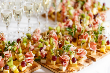 the buffet at the reception. Assortment of canapes on wooden board. Banquet service. catering food, snacks with cheese, jamon, prosciutto and fruit