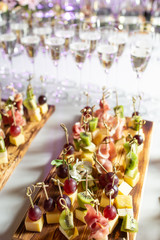 the buffet at the reception. Assortment of canapes on wooden board. Banquet service. catering food, snacks with cheese, jamon, prosciutto and fruit