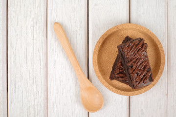 Wooden spoon and chocolate brownie with melted chocolate on a wooden plate