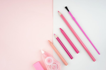 Creative arrangement of stationery such as pencils and brushes on a pastel colored paper. Feminine themed colors like soft red and pink. Flat lay view.