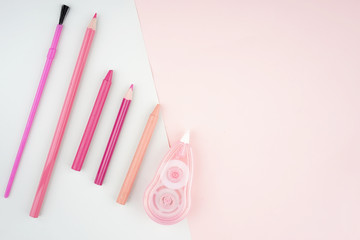 Creative arrangement of stationery such as pencils and brushes on a pastel colored paper. Feminine themed colors like soft red and pink. Flat lay view.