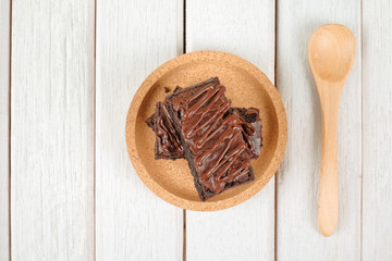 Wooden spoon and chocolate brownie with melted chocolate on a wooden plate