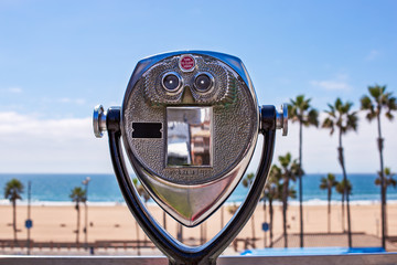 Coin operated binoculars looking out over the ocean and a beach with palm trees.