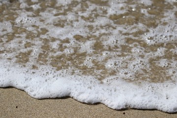 ocean sea foam washing up on a sandy beach 