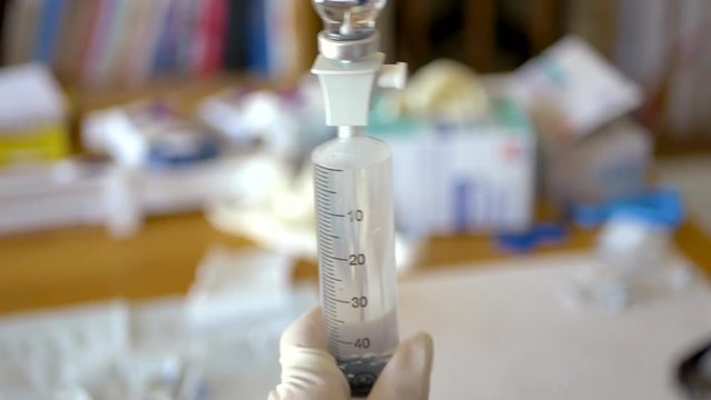 Middle aged woman medical patient preparing vials of antibiotic solution into a large syringe during an at home infusion treatment.