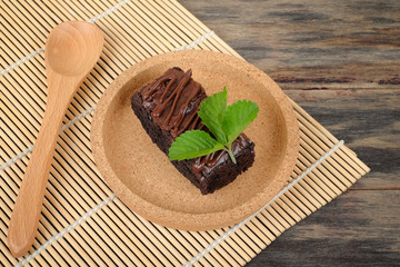 Wooden spoon and chocolate brownie with melted chocolate on a wooden plate