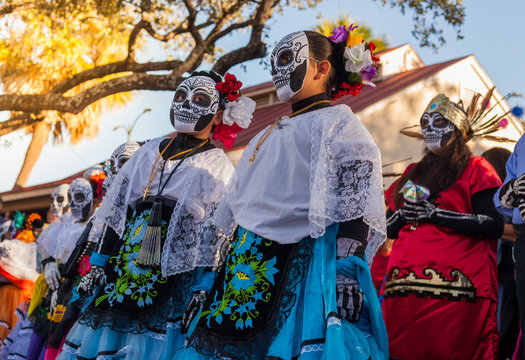 Group of unrecognizable women wearing traditional sugar skull masks and costumes for Dia de los Muertos celebration