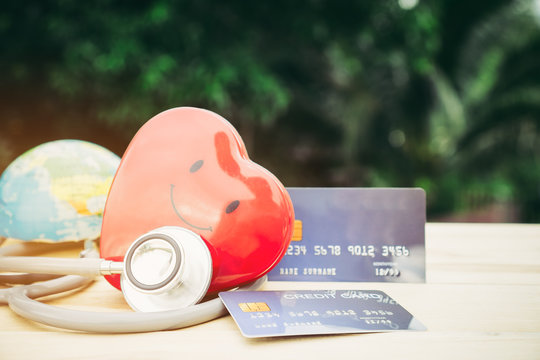 Smile Red Heart Stethoscope On Mock Up Credit Card With Cardholder In Hospital Wood Desk. Concept Of Health Insurance Cost Of Care, Self-care During Illness Using Payments Card For Medicals Service.