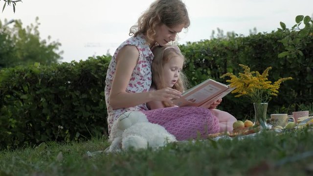 A happy mother and daughter view photos in an album read a book. Family in a city park on a picnic on a warm evening at sunset.