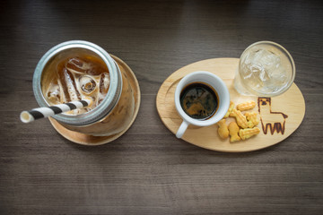 Hot and ice coffee with drinking water and some snack in wooden plate on the wooden table. 