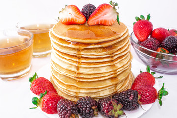 Tasty breakfast. Pancakes with fruit, strawberries and blackberries (mora) pour syrup (honey) on a white background. Close-up.