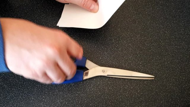 Male with a partially amputated index finger on his right hand cutting strips of white paper diagonally with a pair of blue handled scissor#orrs