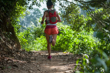 Naklejka na ściany i meble Young woman trail runner running on tropical forest trail