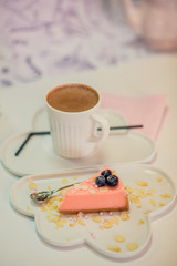 Dessert: pink cheesecake on a white cloud dish, next to a mug of hot chocolate