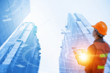 Engineer with safety helmet and tablet on hand looking cover construction building by big crane.