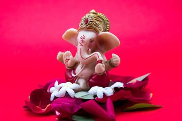 Lord Ganesha Idol with rose petals and white flowers on red background