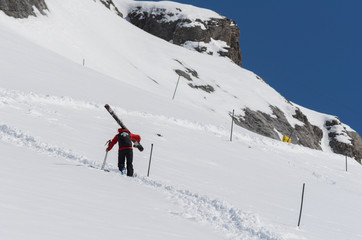 Ski patrol climbing up a mountain slope carrying large skis