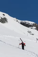 Fotobehang Ski patrol climbing up a mountain slope carrying large skis © Nancy Anderson