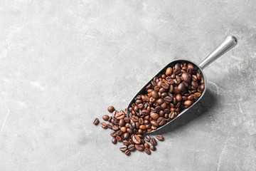 Scoop with roasted coffee beans on grey background, top view. Space for text